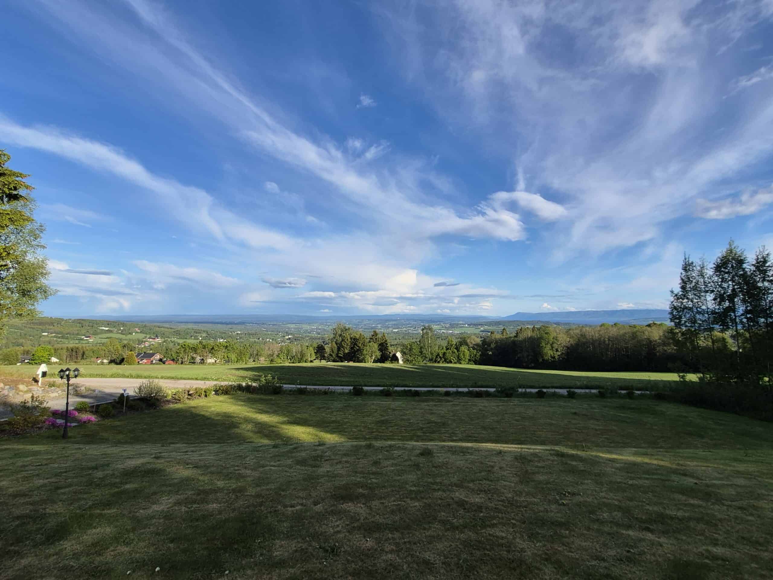 Kystlandskap med åpne grønne områder, trær og en vid himmel med skyer, sett fra et hillside område, ideelt for natur- og landskapsbilde, perfekt for utendørs og reiseinnhold.