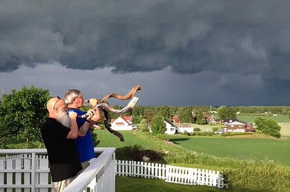 Folk som holder i en stor bjørnebjørn som ser ut til å varmes opp under en mørk himmel over norsk landskap.