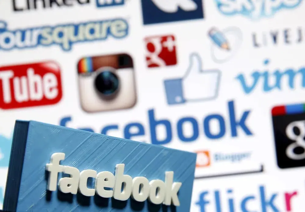 Facebook-logo på en blå bok foran en kollasj av sosiale medie-ikoner, som Instagram, YouTube og Google+, illustrerer digital markedsføring og online tilstedeværelse.